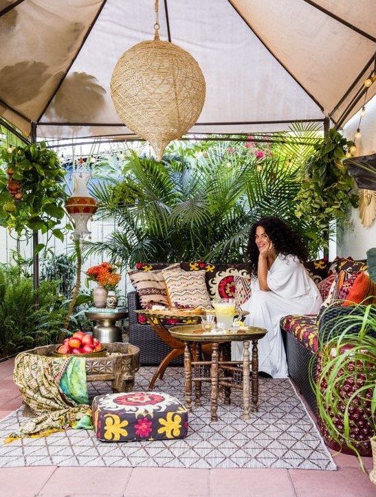 a bright boho tropical patio with a tent on top, boho textiles, colorful pillows and lots of potted plants around