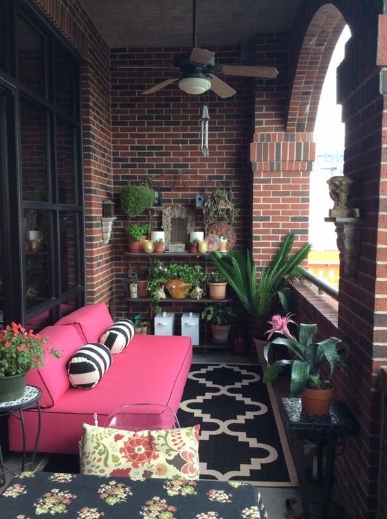a bright small terrace with potted greenery and flowers, a bright pink sofa, patterned pillows and rugs