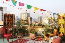 a colorful boho rooftop terrace with bright cushions, pillows and rugs, with bold furniture and lots of potted greenery plus colorful decor