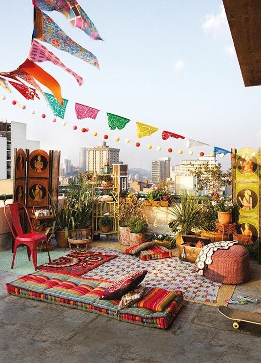a colorful boho rooftop terrace with bright cushions, pillows and rugs, with bold furniture and lots of potted greenery plus colorful decor