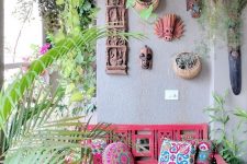 a colorful boho terrace wiht a pink loveseat, colorful pillows, a mask gallery wall and potted greenery and blooms