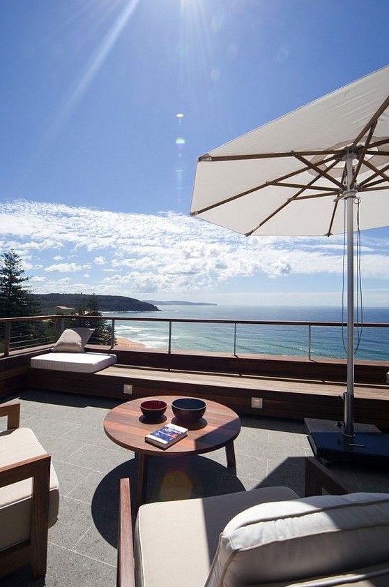 a contemporary beach terrace with neutral chairs, a stained coffee table, a large umbrella and a built in seat plus a gorgeous sea view a contemporary beach terrace with neutral chairs, a stained coffee table, a large umbrella and a built-in seat plus a gorgeous sea view