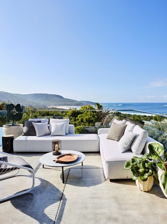 a contemporary coastal terrace with low neutral sofas and pillows, a low coffee table and a leather chair, lots of greenery and a sea view a contemporary coastal terrace with low neutral sofas and pillows, a low coffee table and a leather chair, lots of greenery and a sea view