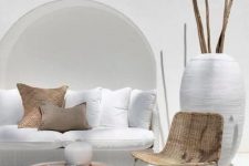 a contemporary neutral terrace with a white wicker sofa in the niche, white pillows, a neutral chair and a whitewashed tree stump table