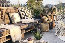 a cool boho terrace with a pallet sofa with printed pillows, a low coffee table, baskets and candle lanterns, potted greenery