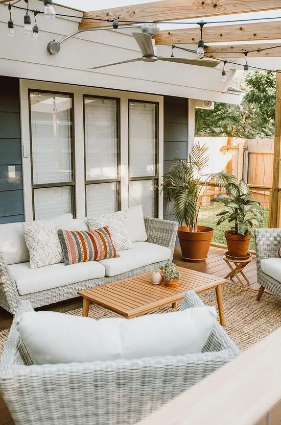 a cool modern country outdoor living room with neutral woven furniture, printed pillows, a wooden table and potted plants welcomes