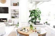 a cool neutral dining space with a corner window, a round table, white chairs, potted greenery and a pendant lamp