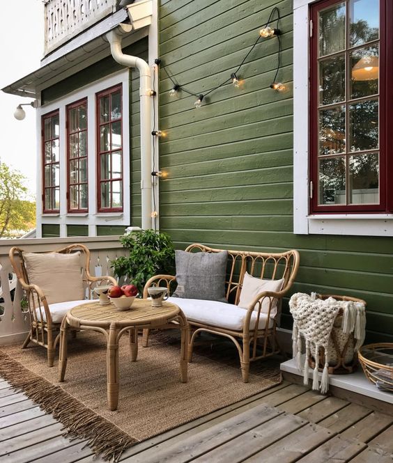 a cozy back porch with rattan furniture and a round table, with neutral upholstery, baskets and string lights is a lovely space