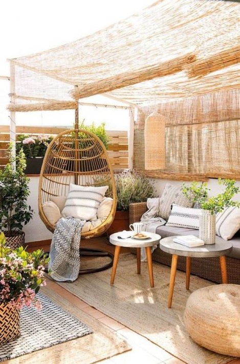a cozy rustic terrrace in natural tones with wicker curtains, wicker furniture, a rattan chair and potted blooms and greenery a cozy rustic terrrace in natural tones with wicker curtains, wicker furniture, a rattan chair and potted blooms and greenery