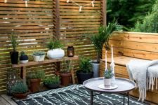 a cozy small terrace with wooden furniture, a small coffee table, a boho rug, potted greenery and lights
