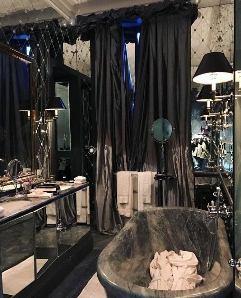 a glam Gothic bathroom with a mirror wall and a mirrored vanity, a grey stone bathtub, black and white textiles and black lamps