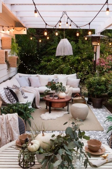 a lively neutral terrace with a corner sofa, a white pendant lamp, greenery and some boho accessories decorated for fall