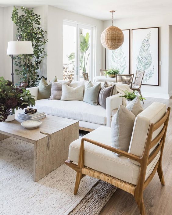 a lovely and welcoming neutral living room with a sofa, some chairs, a plywood coffee table, potted plants, a woven pendant lamp and layered rugs