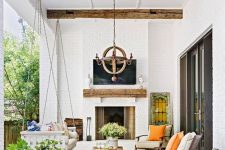 a lovely modern farmhouse terrace with a fireplace, a suspended daybed, modern chairs, potted plants and blooms and a wooden chandelier