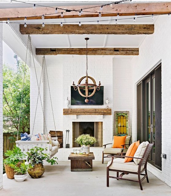 a lovely modern farmhouse terrace with a fireplace, a suspended daybed, modern chairs, potted plants and blooms and a wooden chandelier a lovely modern farmhouse terrace with a fireplace, a suspended daybed, modern chairs, potted plants and blooms and a wooden chandelier