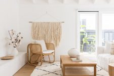 a lovely neutral boho living room with a white sofa, a woven chair and a wooden coffee table, a low built-in bench and a large macrame hanging