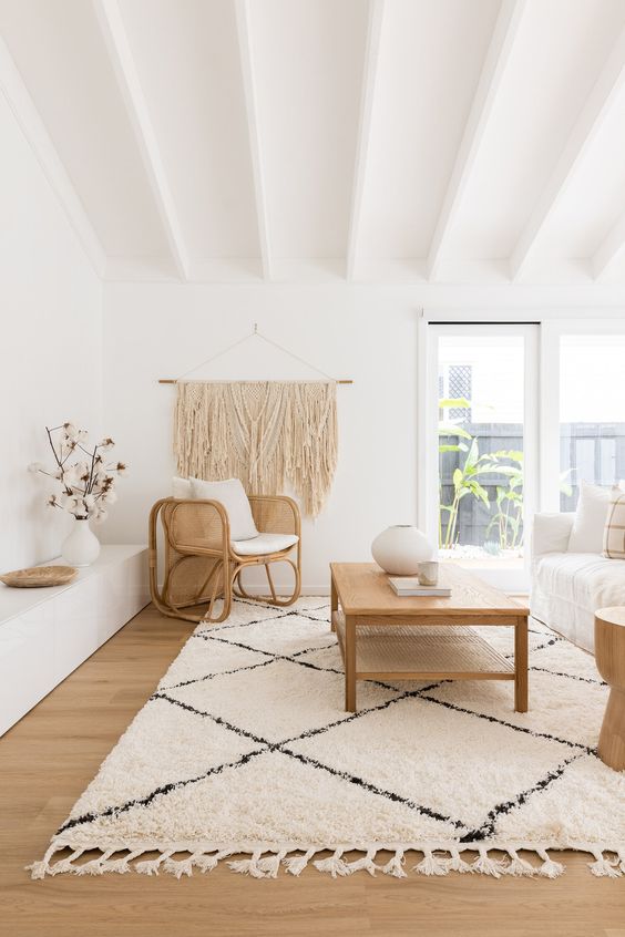 a lovely neutral boho living room with a white sofa, a woven chair and a wooden coffee table, a low built-in bench and a large macrame hanging