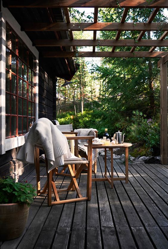 a lovely small Scandinavian porch with light-stained folding furniture, neutral blankets and some tableware on the table