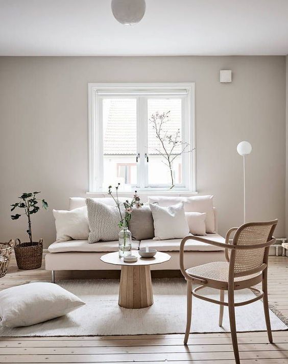 a minimal neutral living room with a blush loveseat, a rattan chair, neutral pillows and some greenery