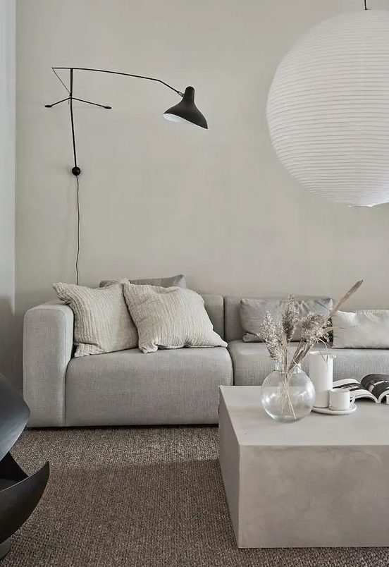 a minimalist greige living room with a grey sofa, a greige stone coffee table, a black sconce and a pendant lamp is amazing