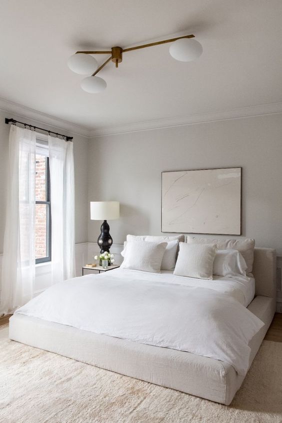 a minimalist neutral bedroom with an upholstered bed, neutral bedding, a retro chandelier and a statement artwork