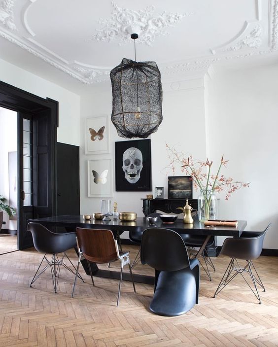 a modern Gothic dining room with white walls and a ceiling, black doors, a black table and chairs plus a pendant lamp