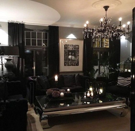 a modern Gothic glam living room with grey walls, black curtains and furniture, a crystal chandelier and candles