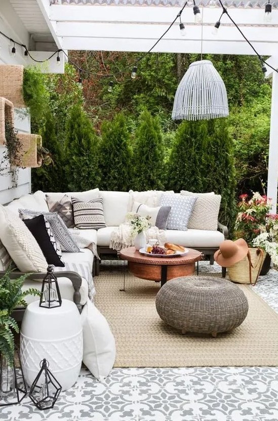 a modern farmhouse patio with a roof, a sectional, a copper coffee table, a woven ottoman, a pendant lamp and some plants