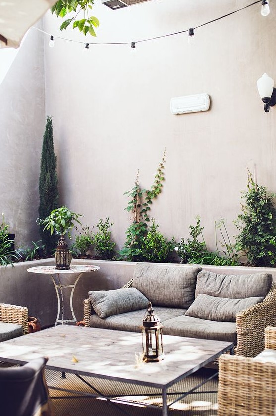 a modern neutral patio with elegant woven furniture, neutral textiles, a side table, los of potted plants and candle lanterns