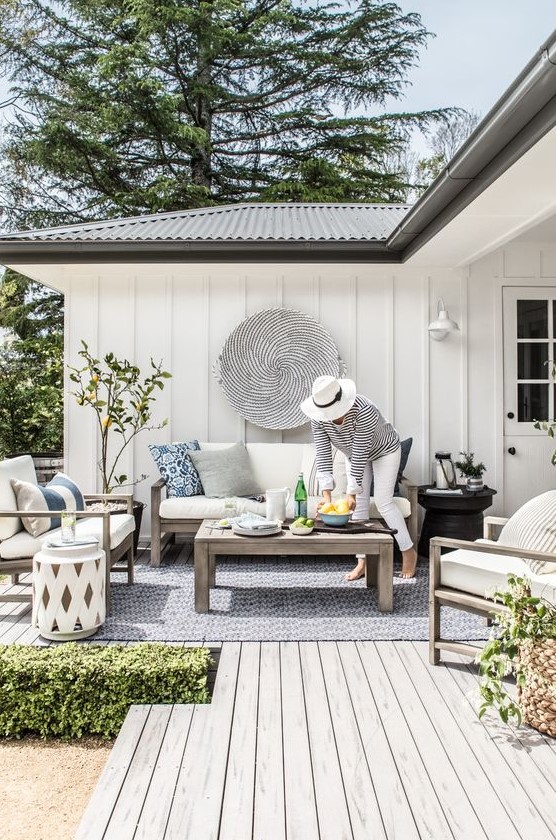a modern neutral terrace with wooden furniture, a printed stool, potted greenery and stools