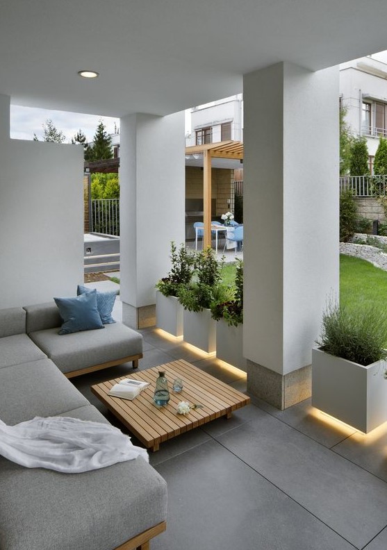 a modern patio with lit up pots with greenery, an L-shaped sofa and a wooden slab table in the center