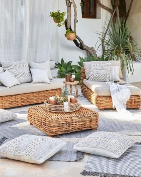 a modern rustic terrace with low wicker furniture, neutral textiles, lots of rugs and throws and greenery