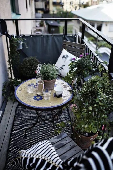 a monochromatic balcony with chairs and a lot of potted greenery is spruced up with a colorful mosaiic table