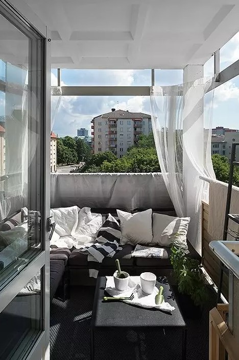 a monochromatic balcony with dark furniture, printed textiles, sheer curtains and potted greenery