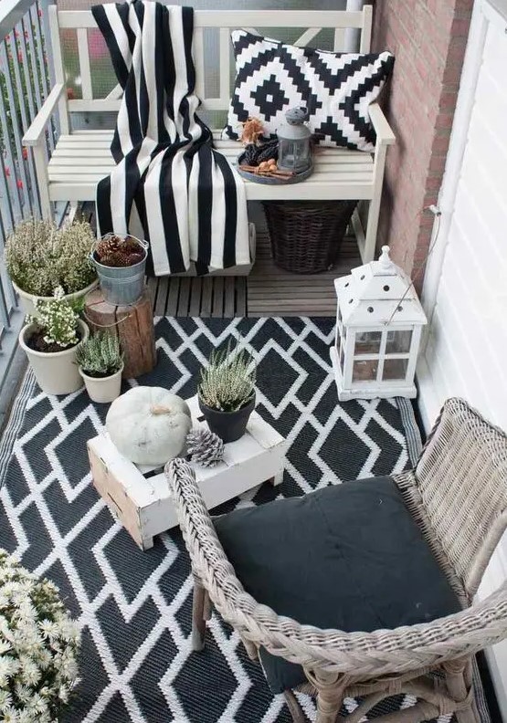 a monochromatic balcony with wicker and wooden furniture, black and white textiles, potted plants and candle lanterns