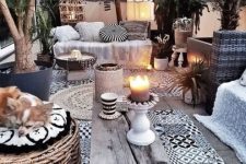a monochromatic boho terrace with printed tiles, a wicker otoman, printed textiles and greenery in pots