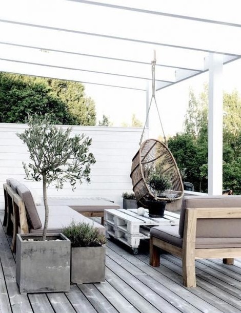 a neutral Scandinavian terrace with simple furniture, a pallet table, a rattan hanging chair and potted greenery