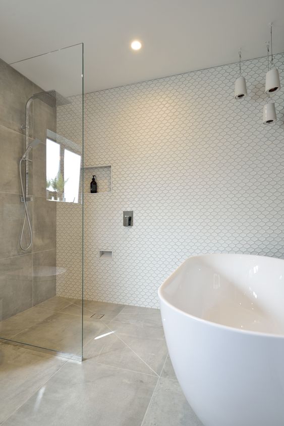 a neutral bathroom with mismatching tiles, an oval tub, a grey tile accent wall, pendant porcelain pendant lamps