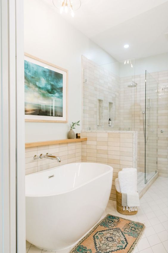 a neutral bathroom with tan tiles, a shower space, an oval tub, a boho rug, a bold artwork and some chrome fixtures is welcoming