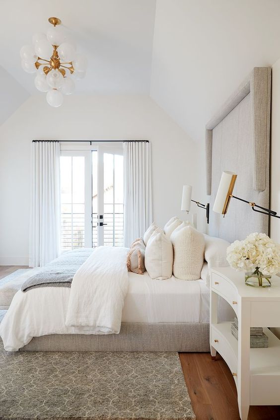 a neutral bedroom with an upholstered bed, neutral bedding, a printed rug and a chic retro chandelier