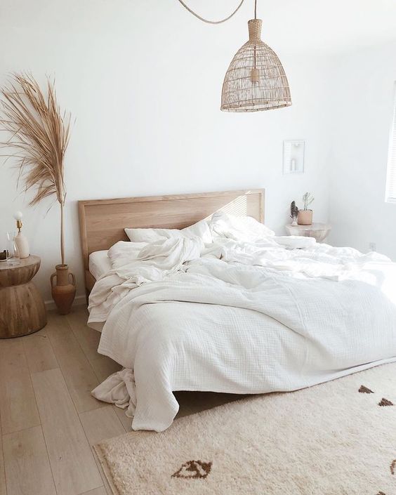 a neutral boho bedroom with wooden furniture and a woven lamp, with pampas grass and neutral bedding is an oasis