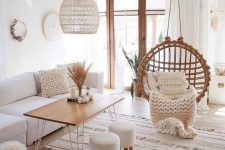 a neutral boho living room with a white sofa, a table with hairpin legs, a pendant chair, lovely rugs and blankets and a pendant lamp