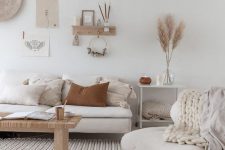 a neutral boho living room with white furniture, a gallery wall, knit items and a woven bench