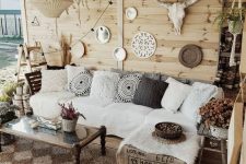 a neutral boho patio with a white corner sofa, a low coffee table, a gallery wall with mirrors and skulls and wovne pendant lamps