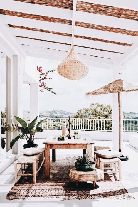 a neutral boho terrace with a wicker lamp, wooden furniture, a jute ottoman and greenery