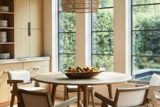 a neutral chic dining room with sleek stained storage units, a round table, some elegant chairs and a woven pendant lamp plus a gorgeous view