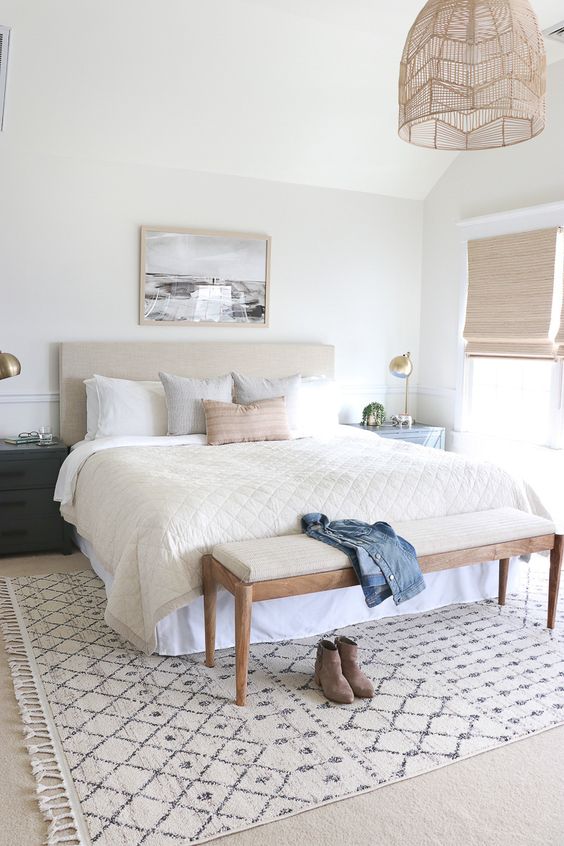 a neutral coastal bedroom with an upholstered bed, woven shades and a lamp, pillows and a long bench