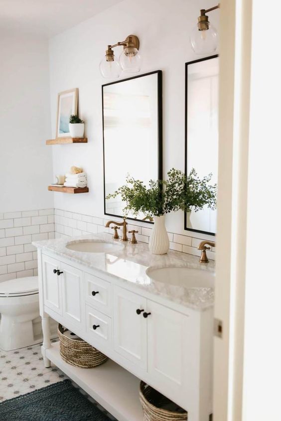 a neutral farmhouse bathroom with subway and printed tiles, a vintage vanity, vintage faucets and a duo of mirrors in sleek frames