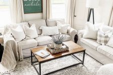 a neutral farmhouse living room with white furniture, a wooden table, neutral curtains, printed textiles