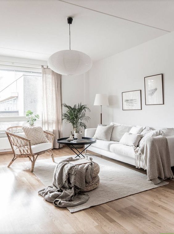 a neutral living room with a white sofa, a rattan chair and wicker ottomans and a catchy black coffee table